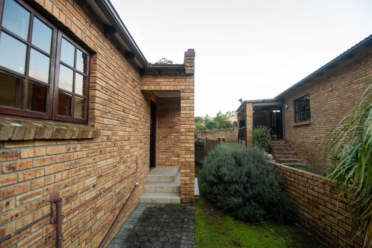 Rear exterior view of a face brick townhouse featuring a paved walkway, entrance steps, and a brick boundary wall.