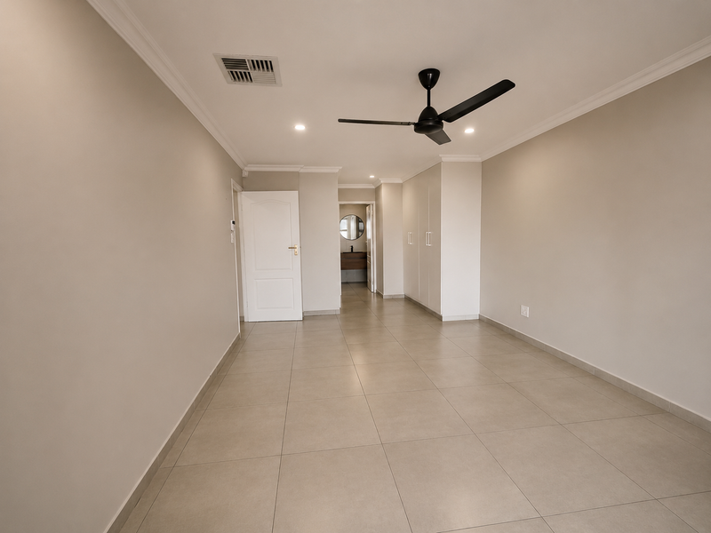 Spacious bedroom featuring neutral tiled flooring, built-in cupboards, a ceiling fan, and ducted air conditioning, with an adjoining ensuite bathroom visible.