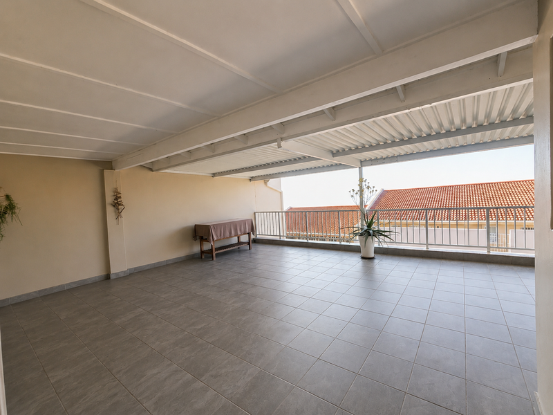 A spacious, covered balcony featuring tiled flooring, a metal balustrade, and an open-air design, offering a versatile outdoor entertainment area.