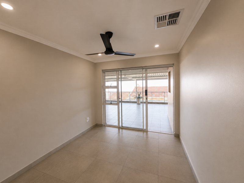 A bright, empty living room featuring neutral tiled flooring, a modern ceiling fan, and large sliding glass doors leading to a covered balcony.