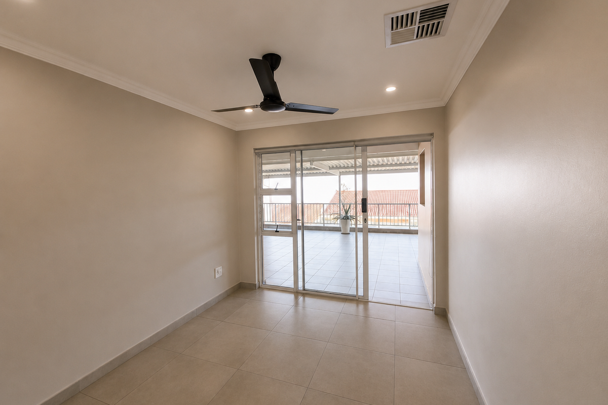 A bright, empty living room featuring neutral tiled flooring, a modern ceiling fan, and large sliding glass doors leading to a covered balcony.