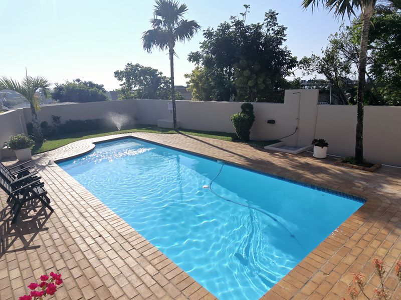 A well-maintained outdoor pool area featuring brick paving, a perimeter wall, and an integrated outdoor shower, perfect for relaxation and recreation.