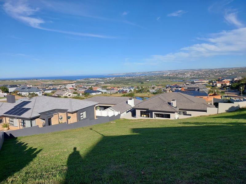 Elevated view overlooking a residential neighborhood with coastal scenery in the distance, showcasing the surrounding landscape and community layout.