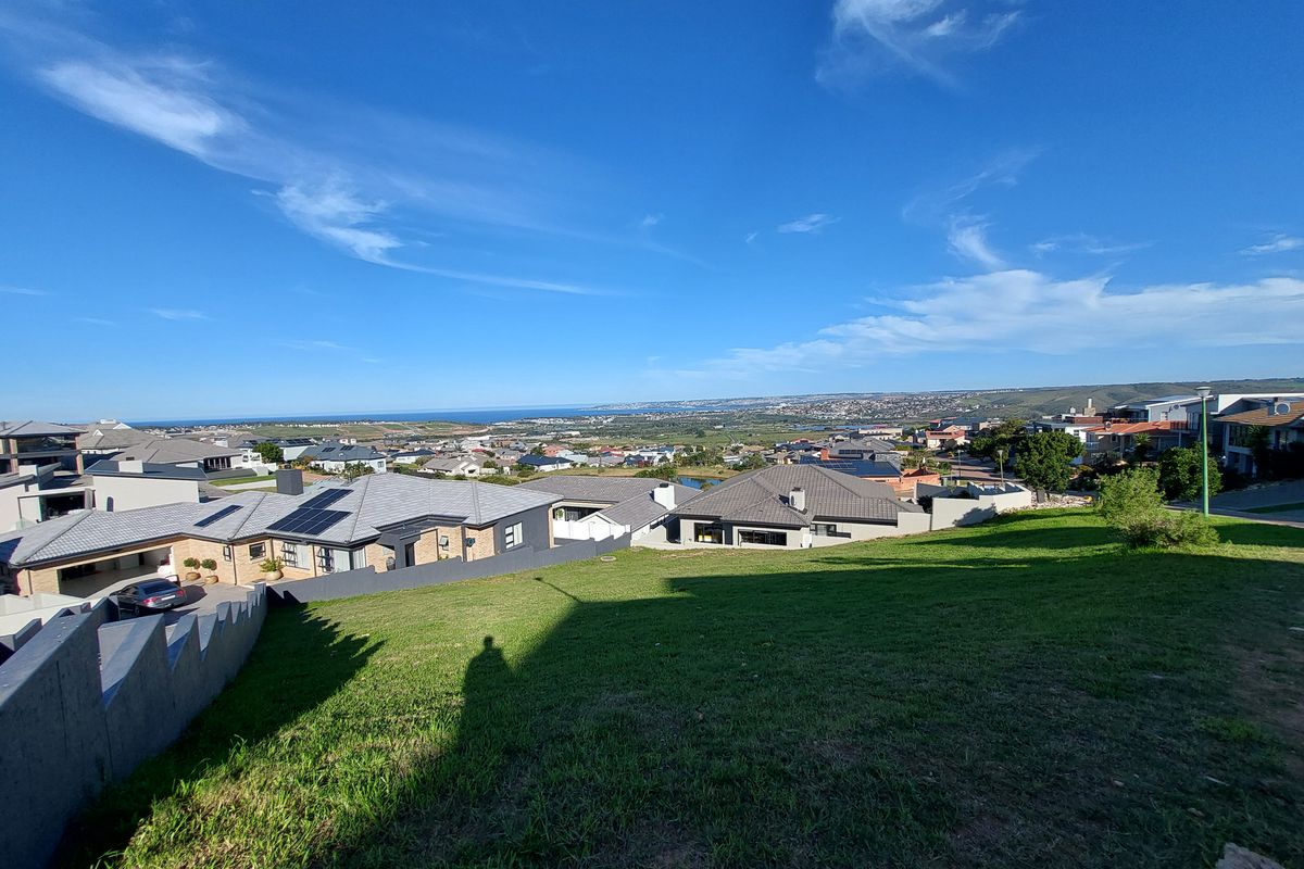 A wide-angle view overlooking a residential neighborhood and distant coastline from a sloped vacant residential plot.