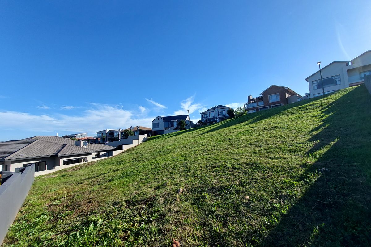 A view of a sloped residential vacant land plot situated in a developed neighborhood with established homes nearby.