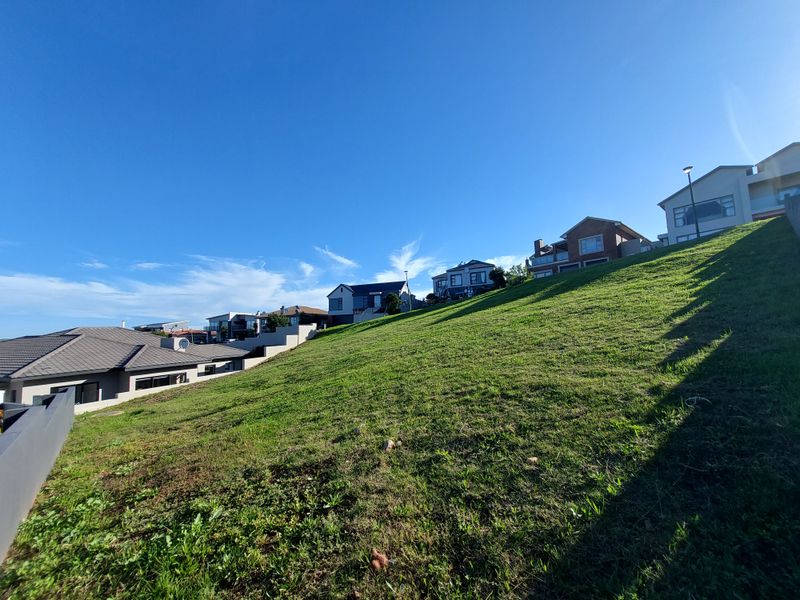 A view of a sloped residential vacant land plot situated in a developed neighborhood with established homes nearby.