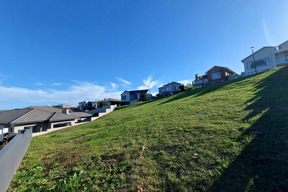 A sloped residential vacant land plot featuring established grass cover, situated in a developed neighborhood with surrounding modern homes.