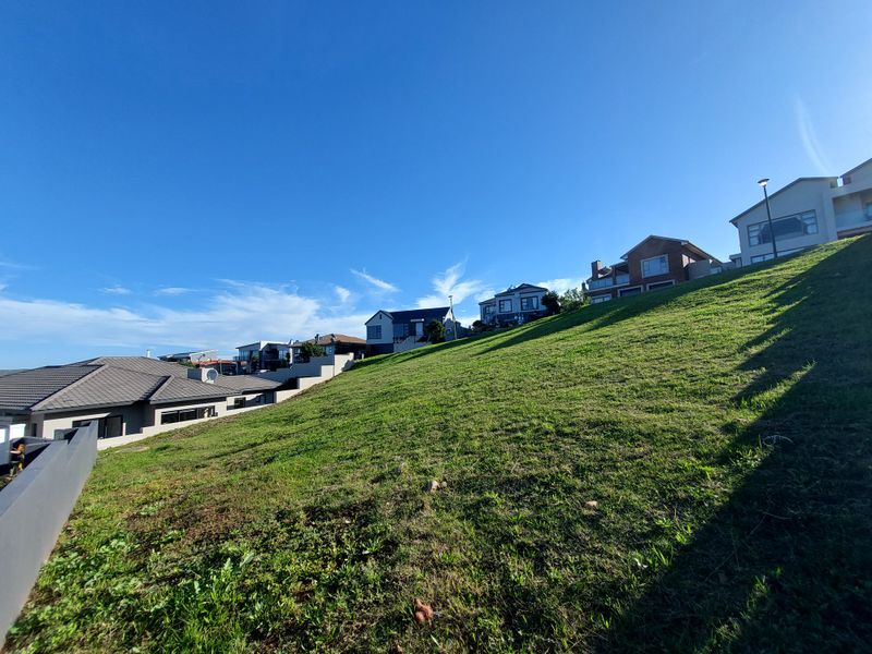 A sloped residential vacant land plot featuring established grass cover, situated in a developed neighborhood with surrounding modern homes.