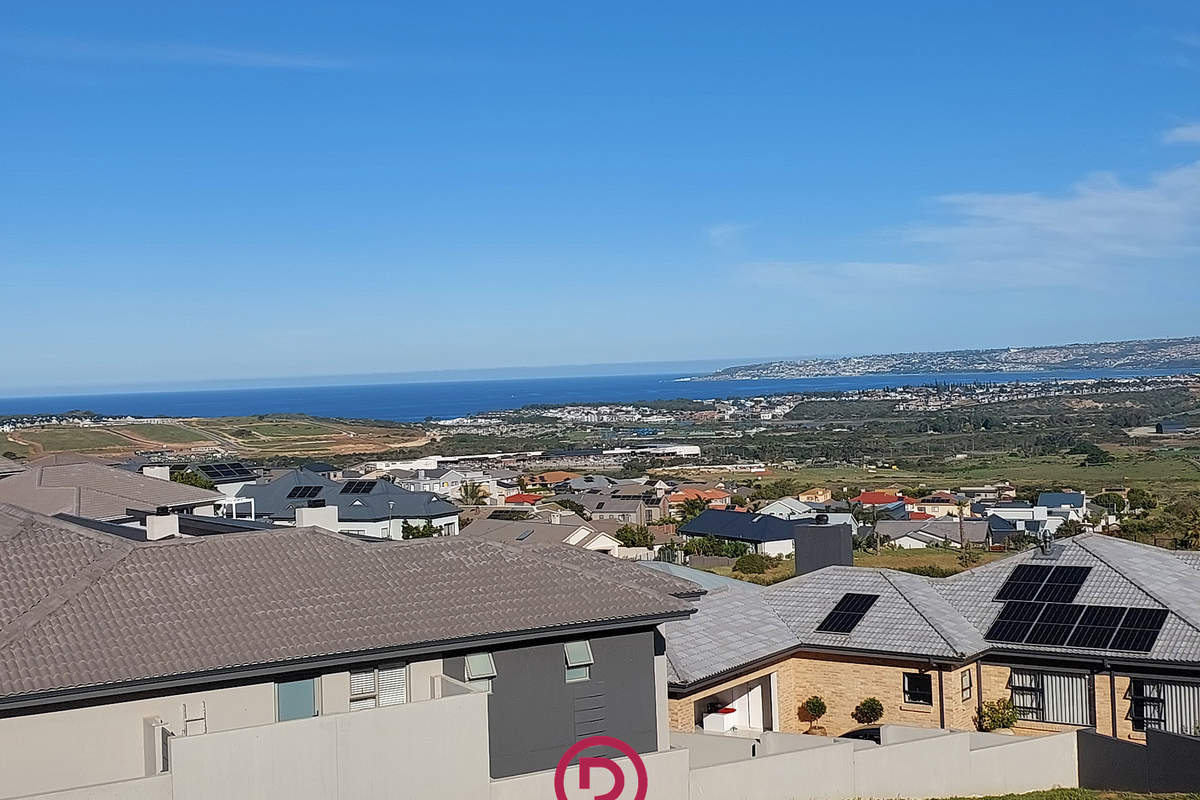 Elevated coastal view overlooking a residential neighborhood with distant ocean scenery and clear blue skies.