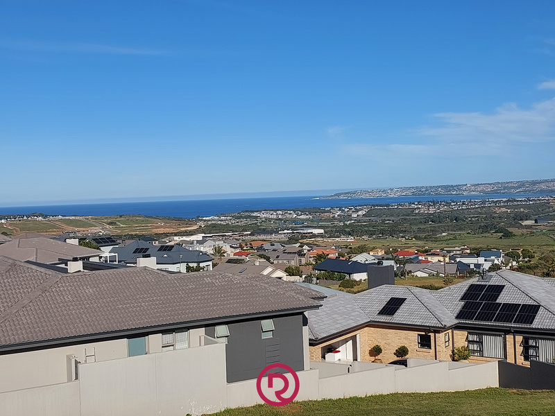 Elevated coastal view overlooking a residential neighborhood with distant ocean scenery and clear blue skies.