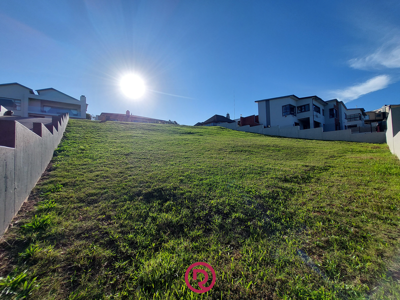 A vacant residential plot featuring a sloped grassy surface and established concrete retaining walls, situated within a developed neighborhood.