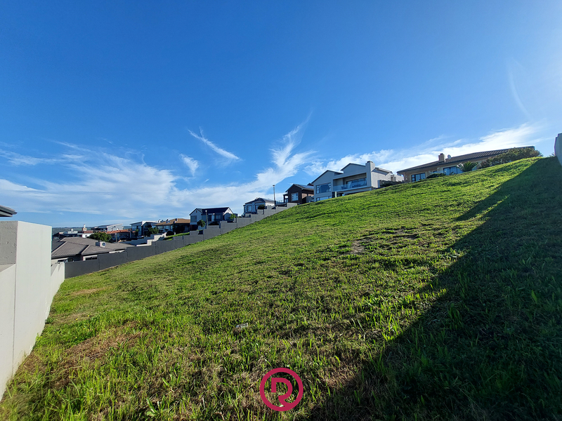 A sloped residential vacant land plot featuring a concrete retaining wall, situated in an established neighborhood with surrounding homes.