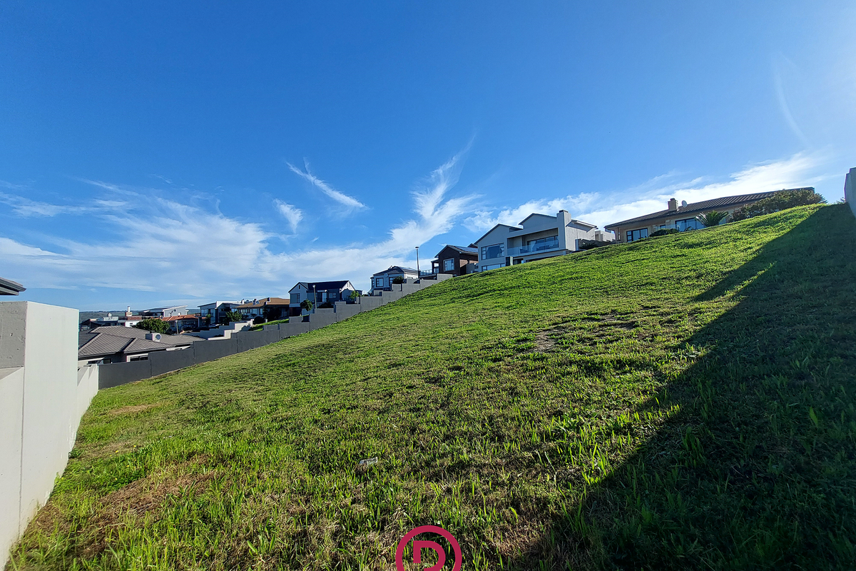 A sloped residential vacant land plot featuring a concrete retaining wall, situated in an established neighborhood with surrounding homes.