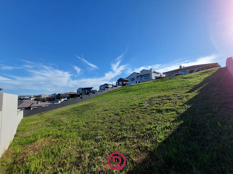 A sloped residential vacant land plot featuring a retaining wall and established grass, situated in a developed neighborhood.