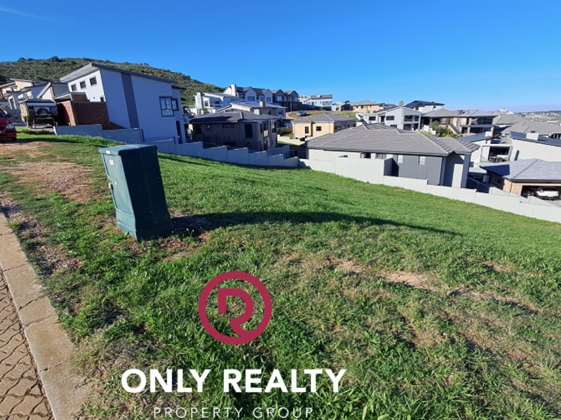 A vacant residential plot situated in a developed estate, featuring a grassed surface and direct access to a paved street.