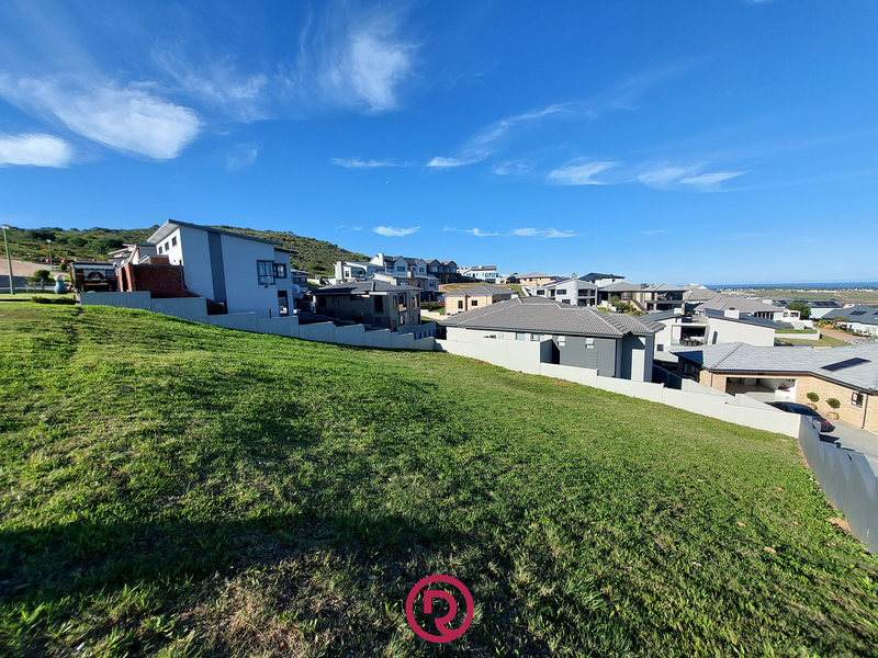 A sloping vacant residential plot featuring established boundary walls and views of the surrounding neighborhood and distant coastline.