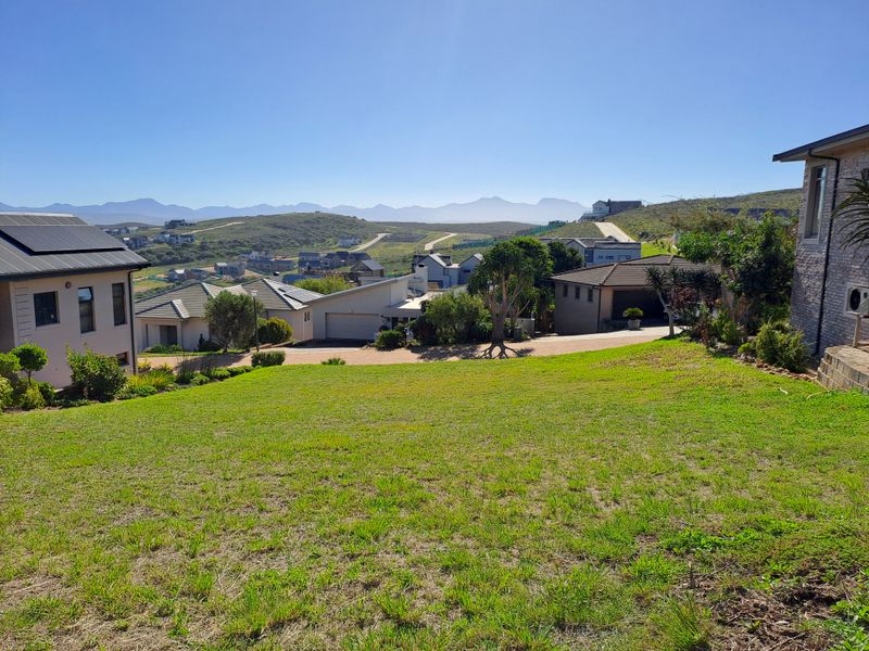 A scenic view overlooking a residential estate with sloped green terrain and distant mountain vistas.