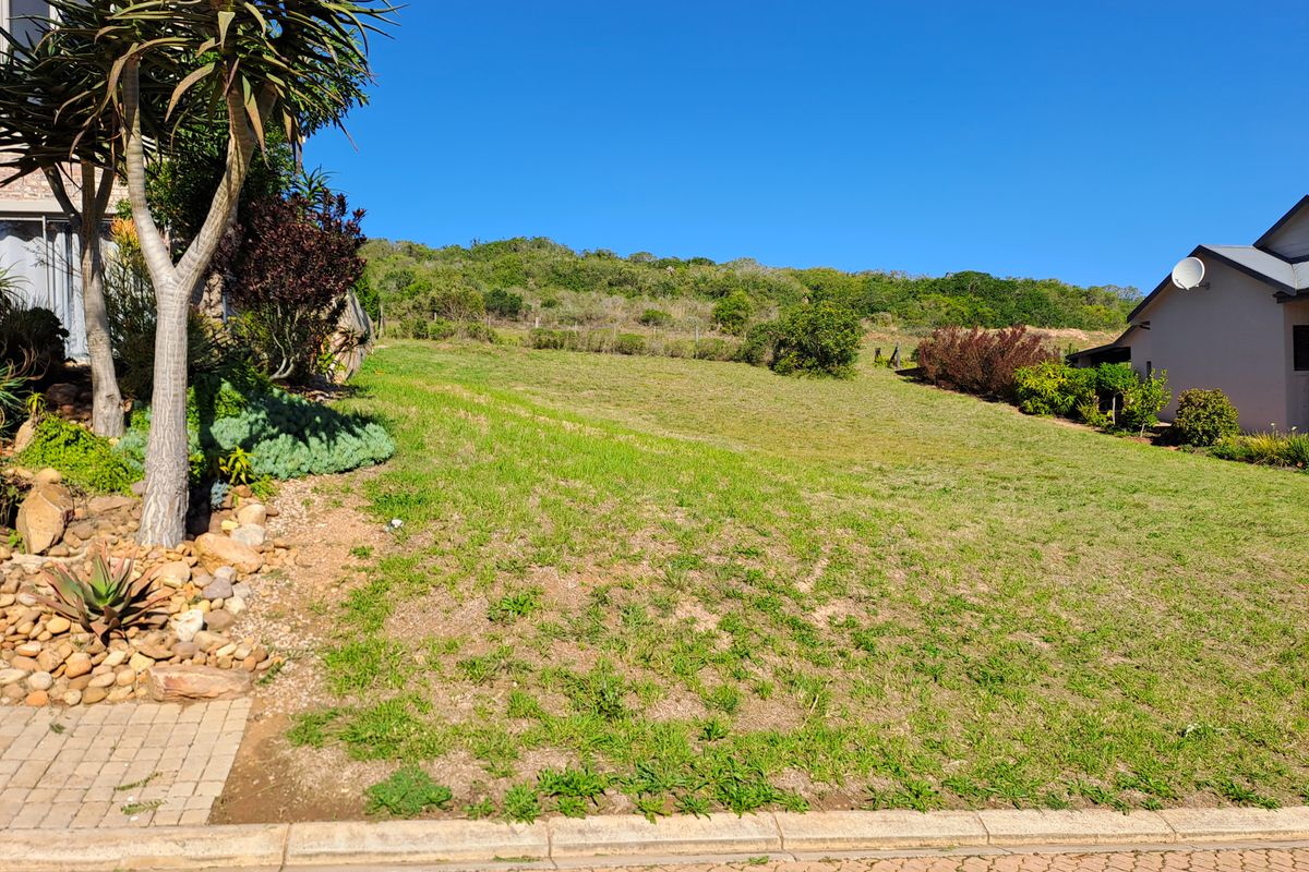 A vacant residential plot featuring a gentle upward slope, established rockery landscaping, and paved street frontage in a quiet neighborhood setting.