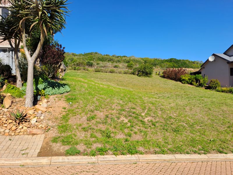 A vacant residential plot featuring a gentle upward slope, established rockery landscaping, and paved street frontage in a quiet neighborhood setting.