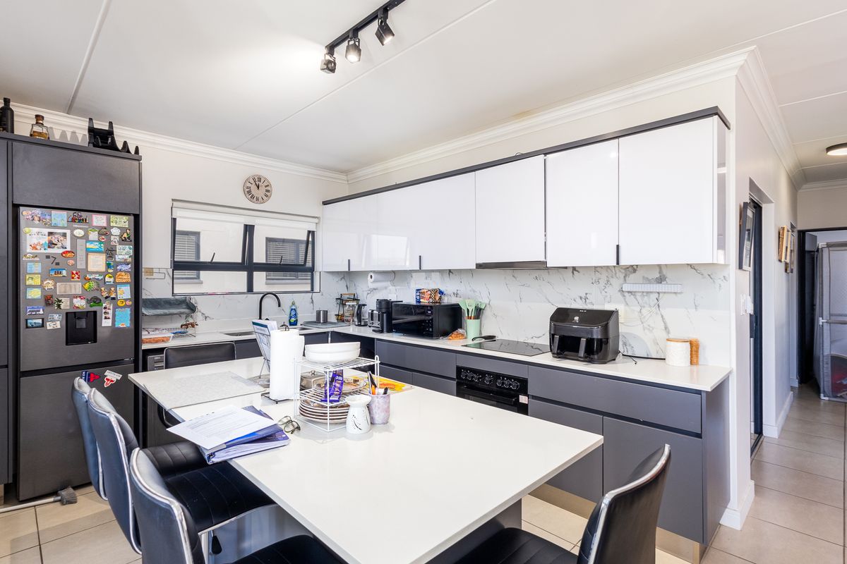 Modern kitchen featuring high-gloss cabinetry, stone countertops, marble-look splashback, integrated oven, and a central island with breakfast bar seating.
