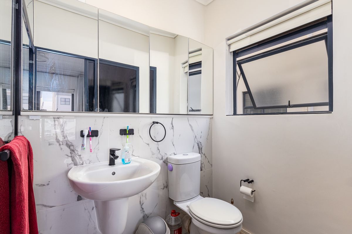 A clean, modern bathroom featuring marble-look wall tiles, a pedestal basin, a toilet, and a functional mirrored medicine cabinet.