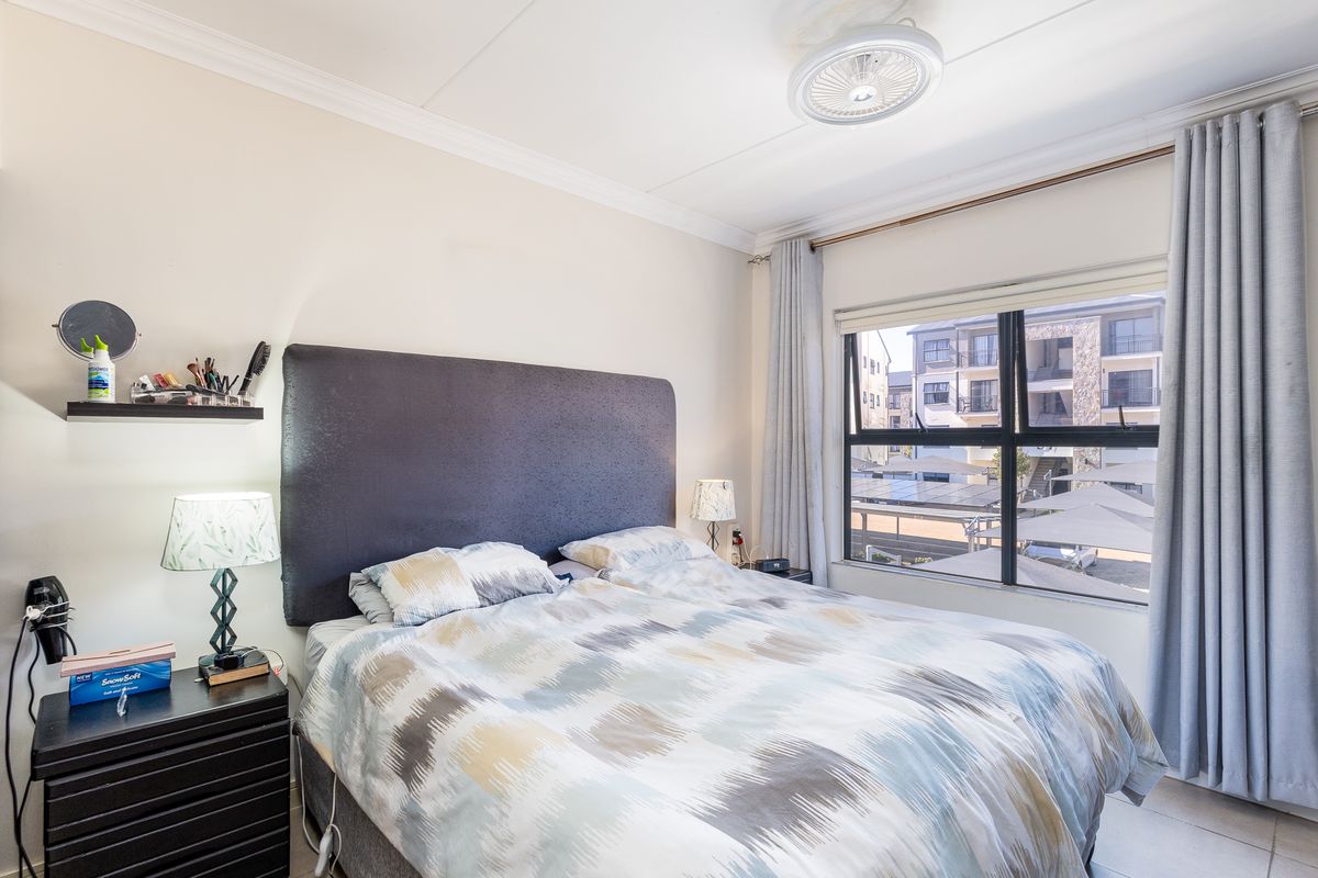 A well-lit bedroom featuring a ceiling fan, large aluminium-framed window with curtain tracks, and neutral wall finishes.