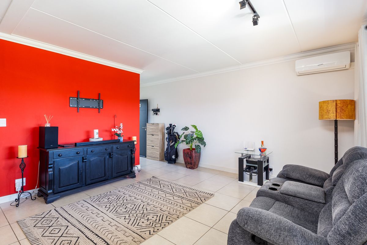 A bright living room featuring tiled flooring, a wall-mounted TV bracket, and a wall-mounted air conditioning unit.