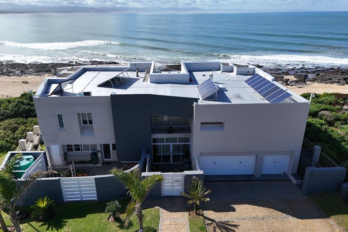 Aerial view of a modern beachfront property featuring solar panels, a double garage, and a paved driveway with direct ocean access.