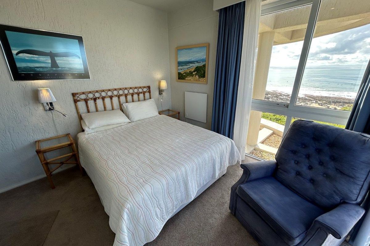 A bedroom featuring textured walls, carpeted flooring, and a large sliding glass door providing direct access to a balcony with ocean views.