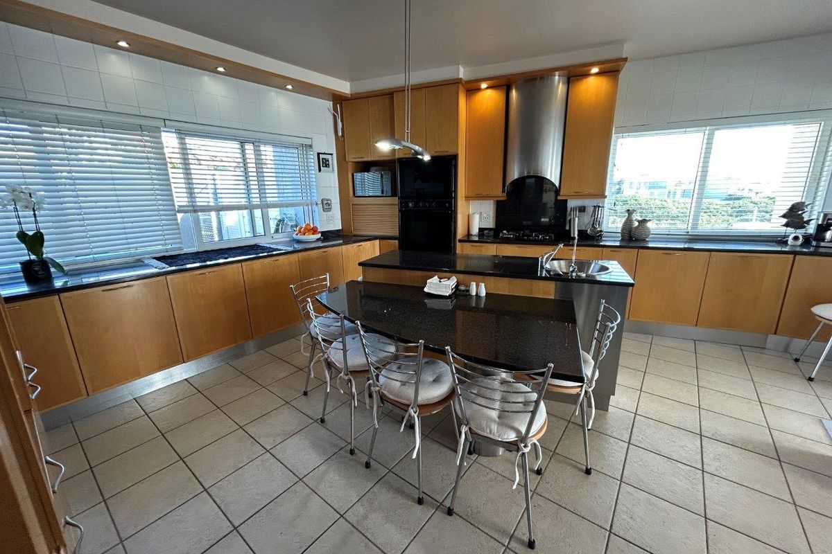 Spacious kitchen featuring light wood cabinetry, granite countertops, a central island, and integrated appliances, finished with ceramic floor tiles.