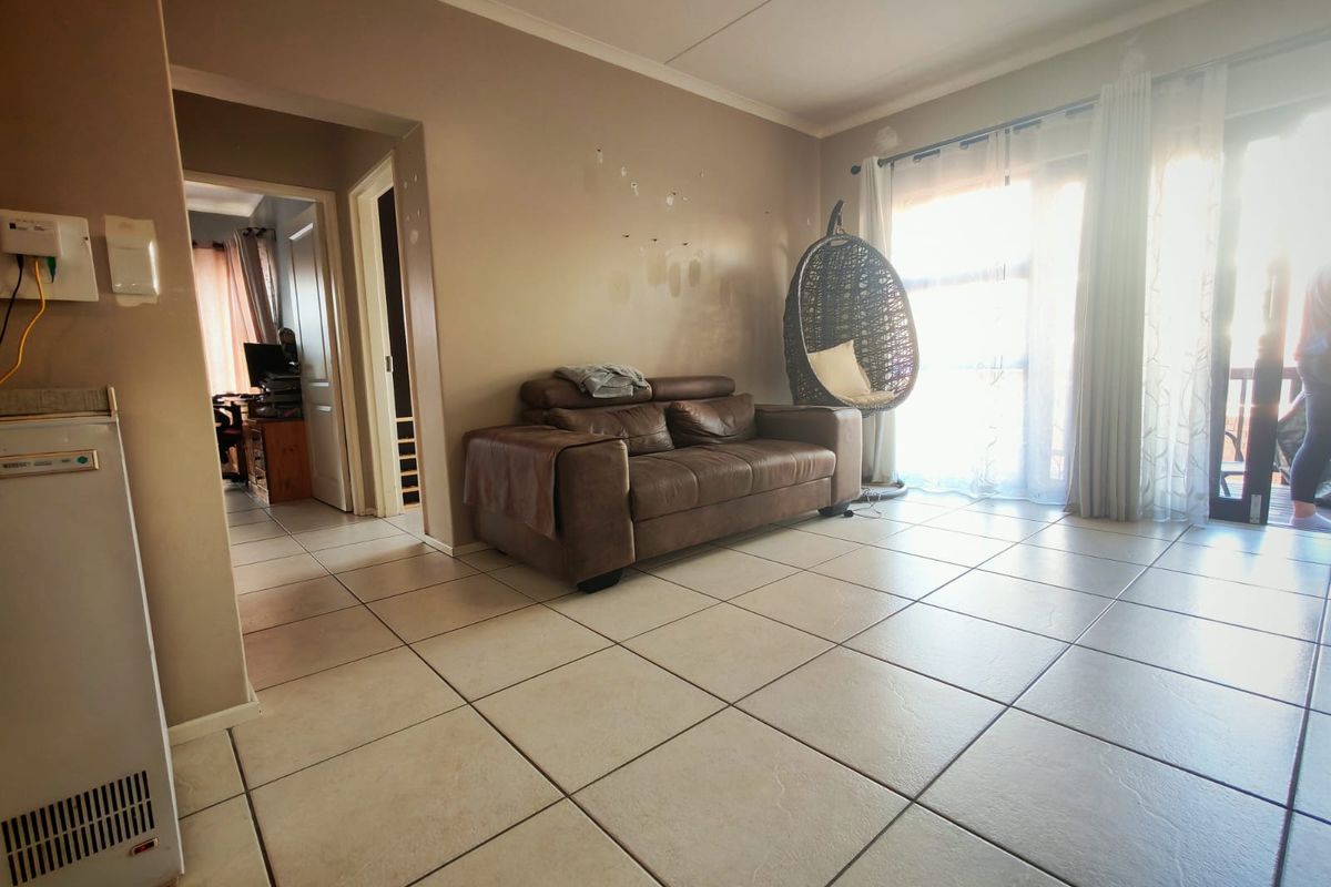 Spacious living area featuring neutral tiled flooring, a built-in wall heater, and large sliding glass doors providing access to the outdoor area.