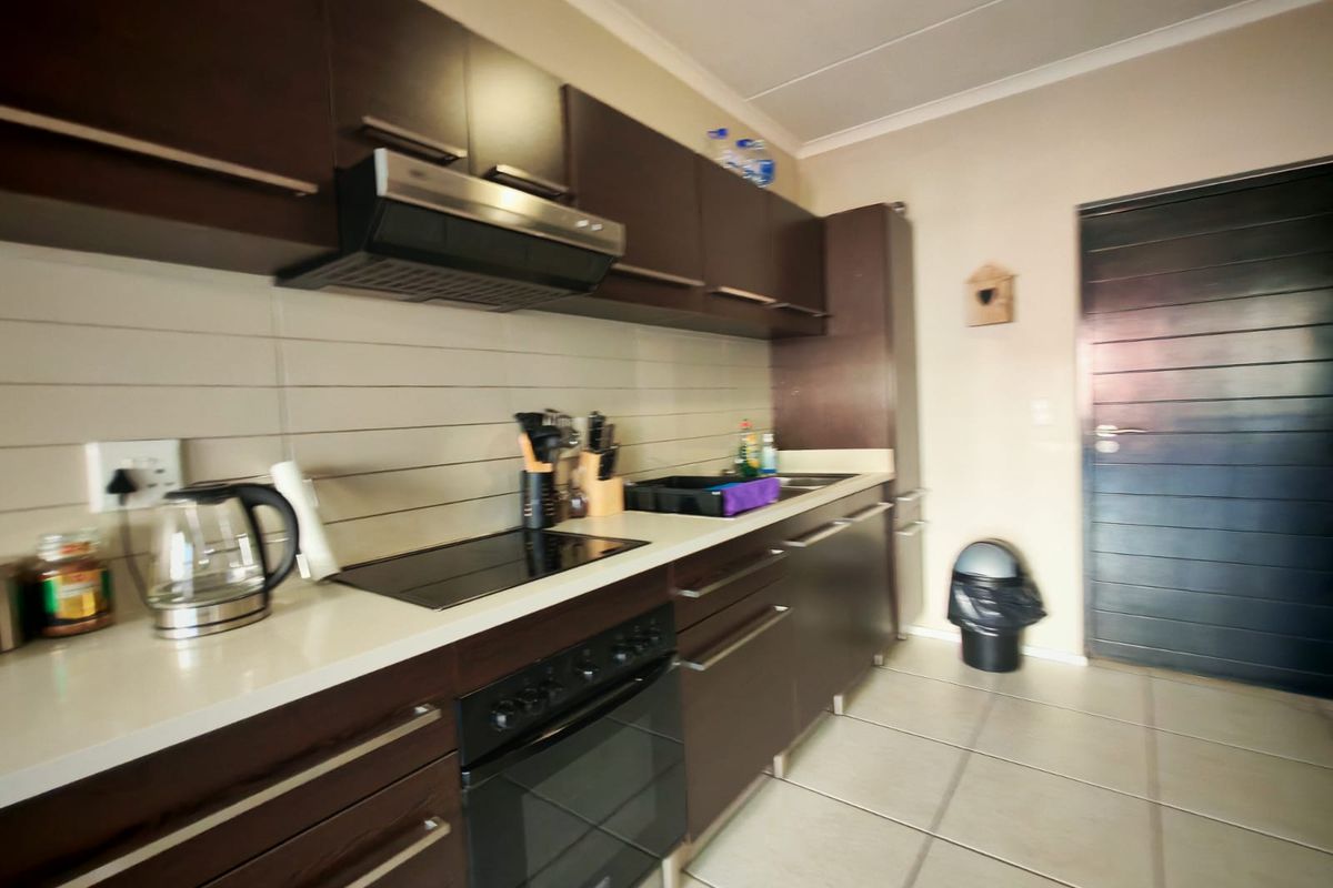 A functional kitchen featuring dark wood cabinetry, white stone countertops, built-in oven, electric hob, and tiled flooring.
