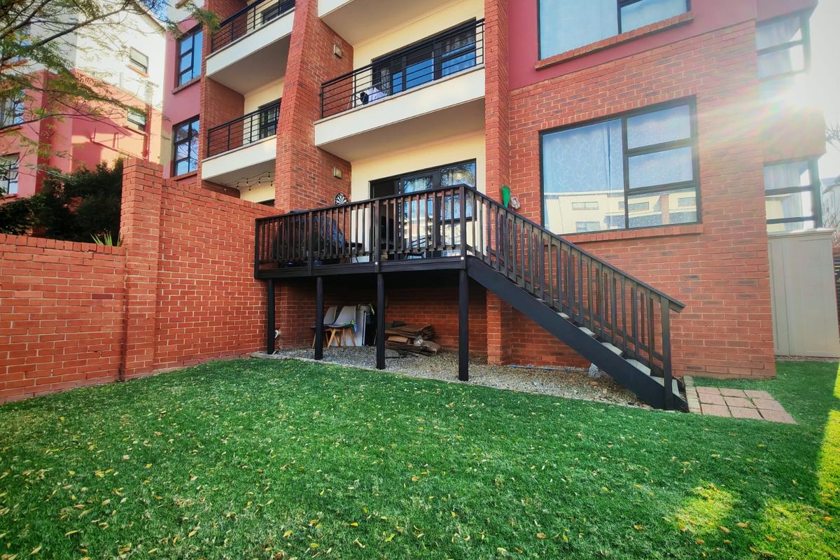 Rear view of the apartment building featuring a private garden, a raised timber deck with stairs, and brick exterior finishes.