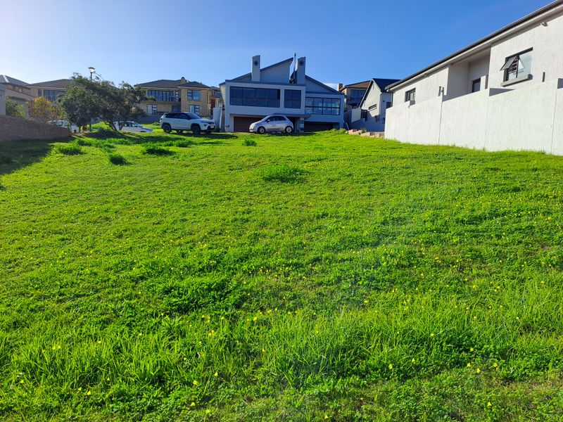 A vacant residential plot featuring a gentle slope and established grass cover, situated in a developed neighborhood.