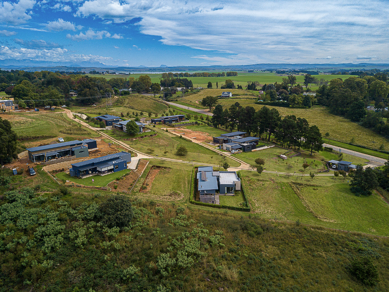 Aerial view of a residential development featuring modern dwellings set within a spacious, landscaped rural estate with established road access.