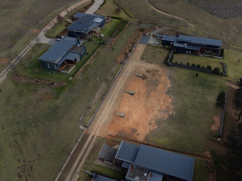 Aerial view of a vacant residential plot featuring an access road and surrounding established properties in a rural estate setting.