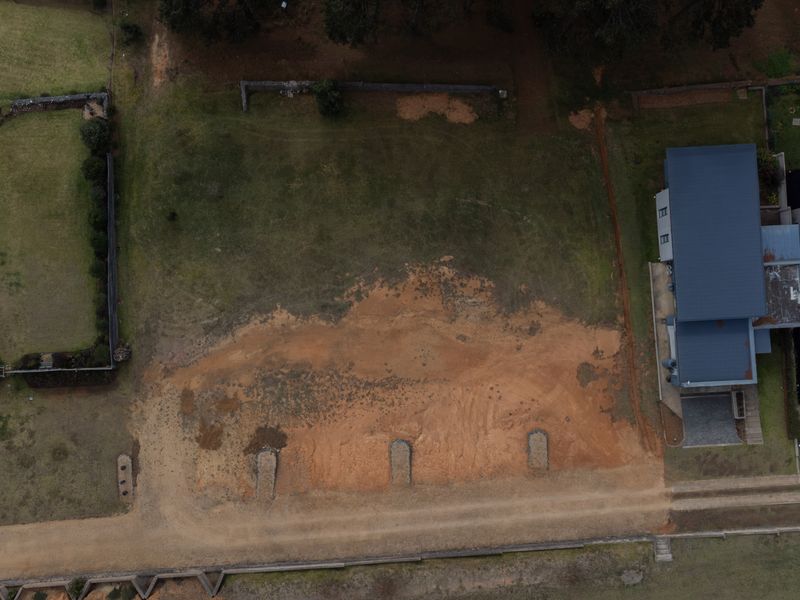 Aerial view of a vacant residential plot situated between existing properties, featuring open grass and exposed soil areas.