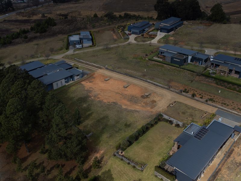 Aerial view of a vacant residential plot situated within an established estate, featuring surrounding modern homes and access infrastructure.
