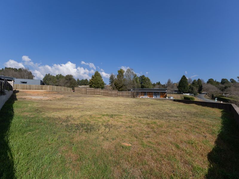 A spacious, open residential plot featuring established grass, perimeter timber fencing, and concrete retaining walls.