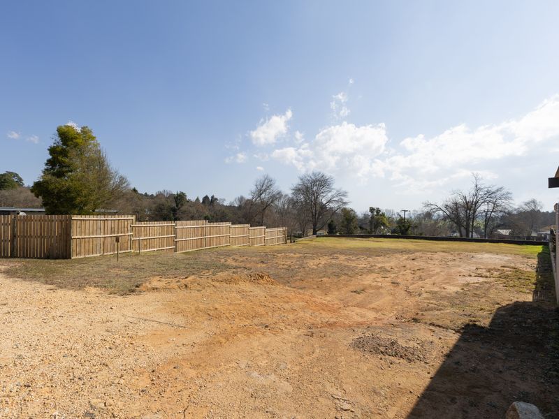 A spacious, vacant residential land parcel featuring a gravel driveway, perimeter timber fencing, and a water tank, offering a blank canvas for development.