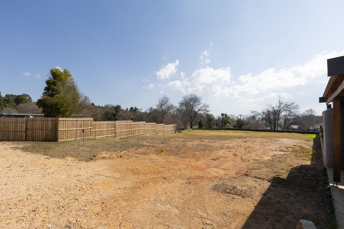 A spacious, vacant residential land parcel featuring a gravel driveway, perimeter timber fencing, and a water tank, offering a blank canvas for development.
