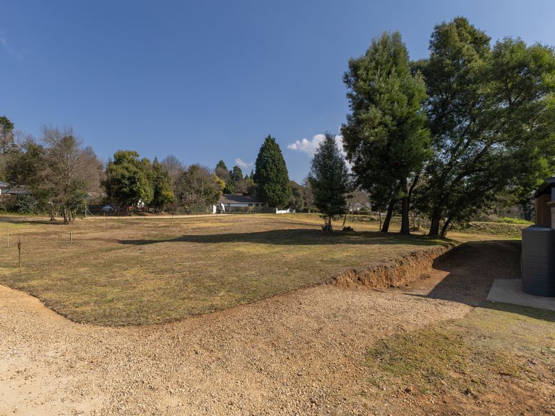 A spacious residential plot featuring a gravel driveway, mature trees, and a water tank, offering a clear area for potential development.