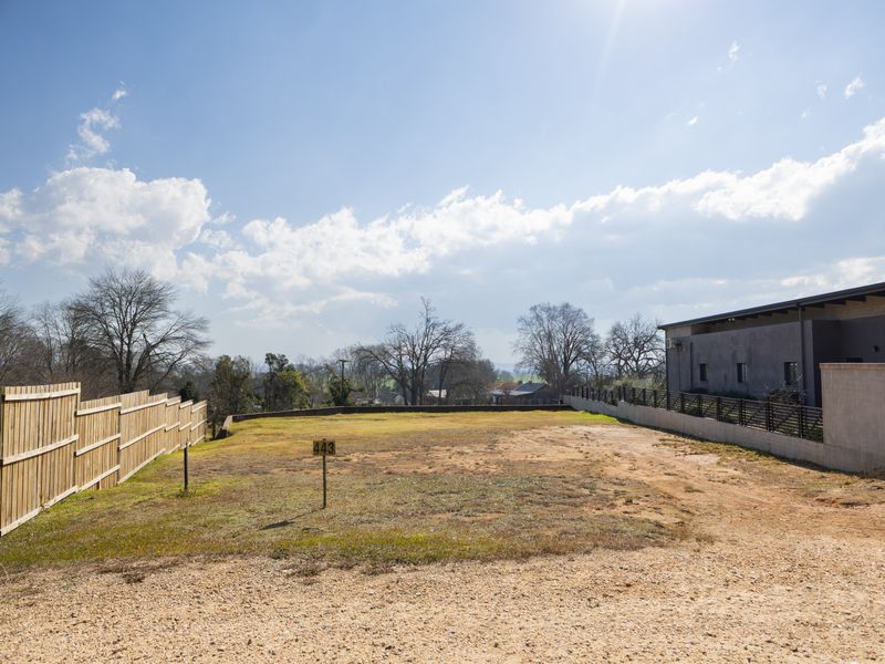 A vacant residential plot featuring a gravel driveway, timber and metal boundary fencing, and a retaining wall, ready for development.