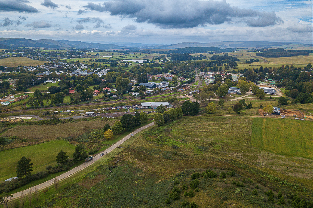 An aerial view of the surrounding rural landscape, featuring local road and rail infrastructure with expansive green fields and distant town development.