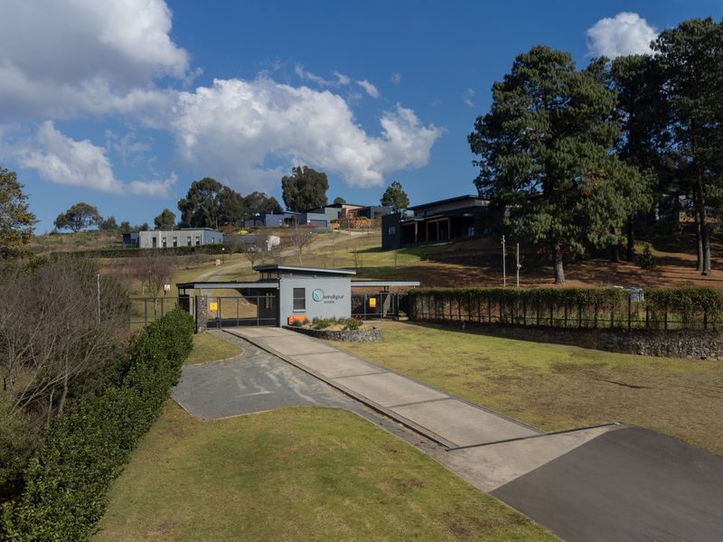 Aerial view of the secure estate entrance featuring a modern gatehouse, paved driveway, and well-maintained landscaped grounds with mature trees.