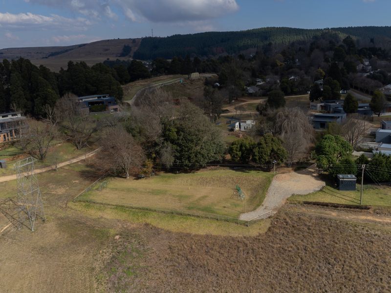 Aerial view of a vacant residential plot featuring a fenced area, gravel driveway, and surrounding landscape in a rural estate setting.