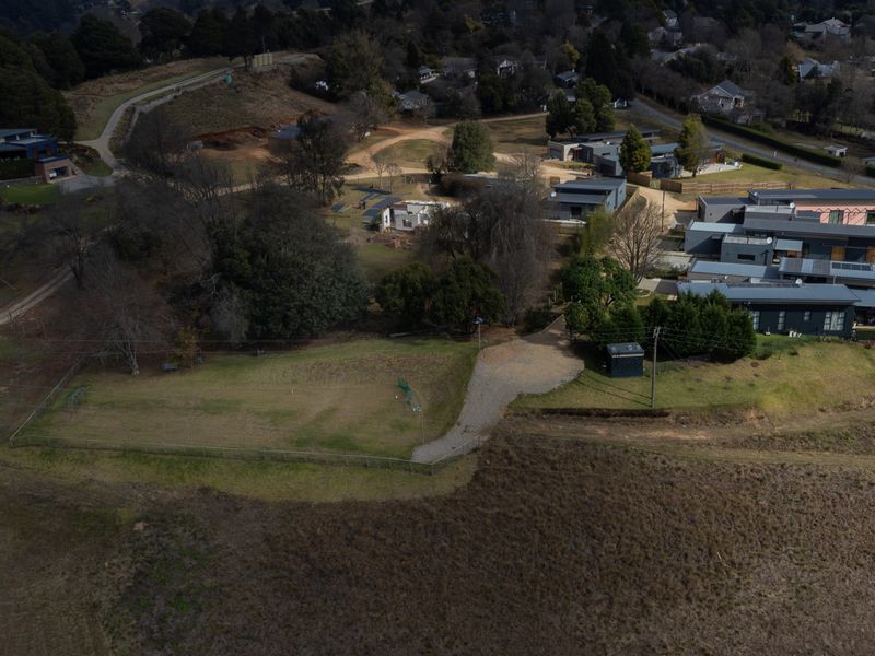An aerial view of a vacant residential plot featuring a gravel driveway, perimeter fencing, and surrounding established residential properties.