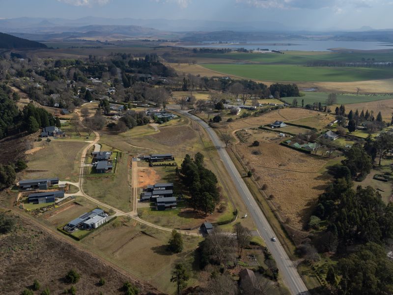 An aerial view of a residential area featuring scattered modern homes, open land, and surrounding rural landscape with a main road running through.