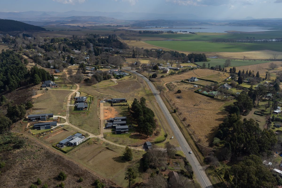 An aerial view of a residential area featuring scattered modern homes, open land, and surrounding rural landscape with a main road running through.