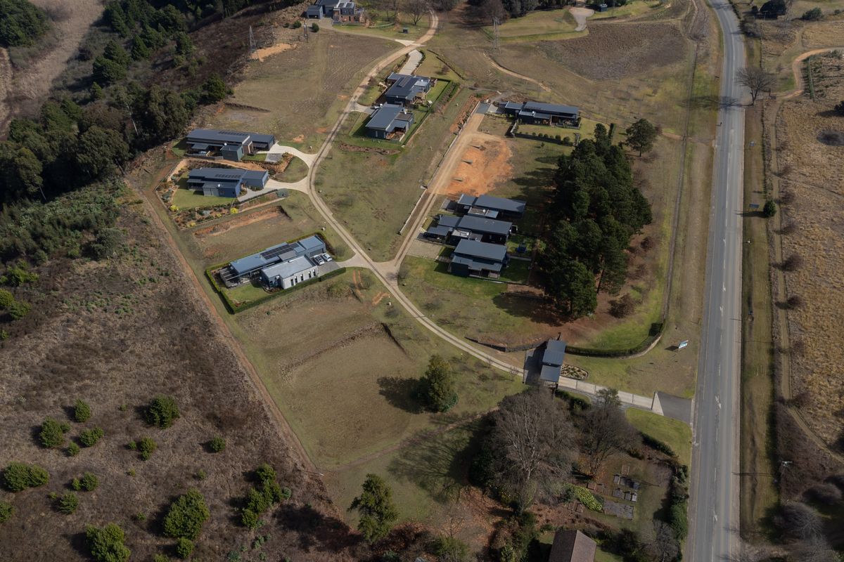 An aerial view of a residential estate featuring multiple modern dwellings, internal access roads, and surrounding natural landscape.